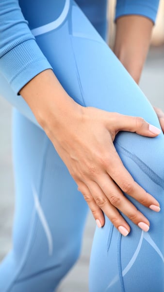 KI Bild welches die Nahaufnahme einer Frau in hellblauen Sport-Leggings darstellt, die sich mit beiden Händen an das schmerzende Knie fasst. KI Bild welches die Nahaufnahme einer Frau in hellblauen Sport-Leggings darstellt, die sich mit beiden Händen an das schmerzende Knie fasst.